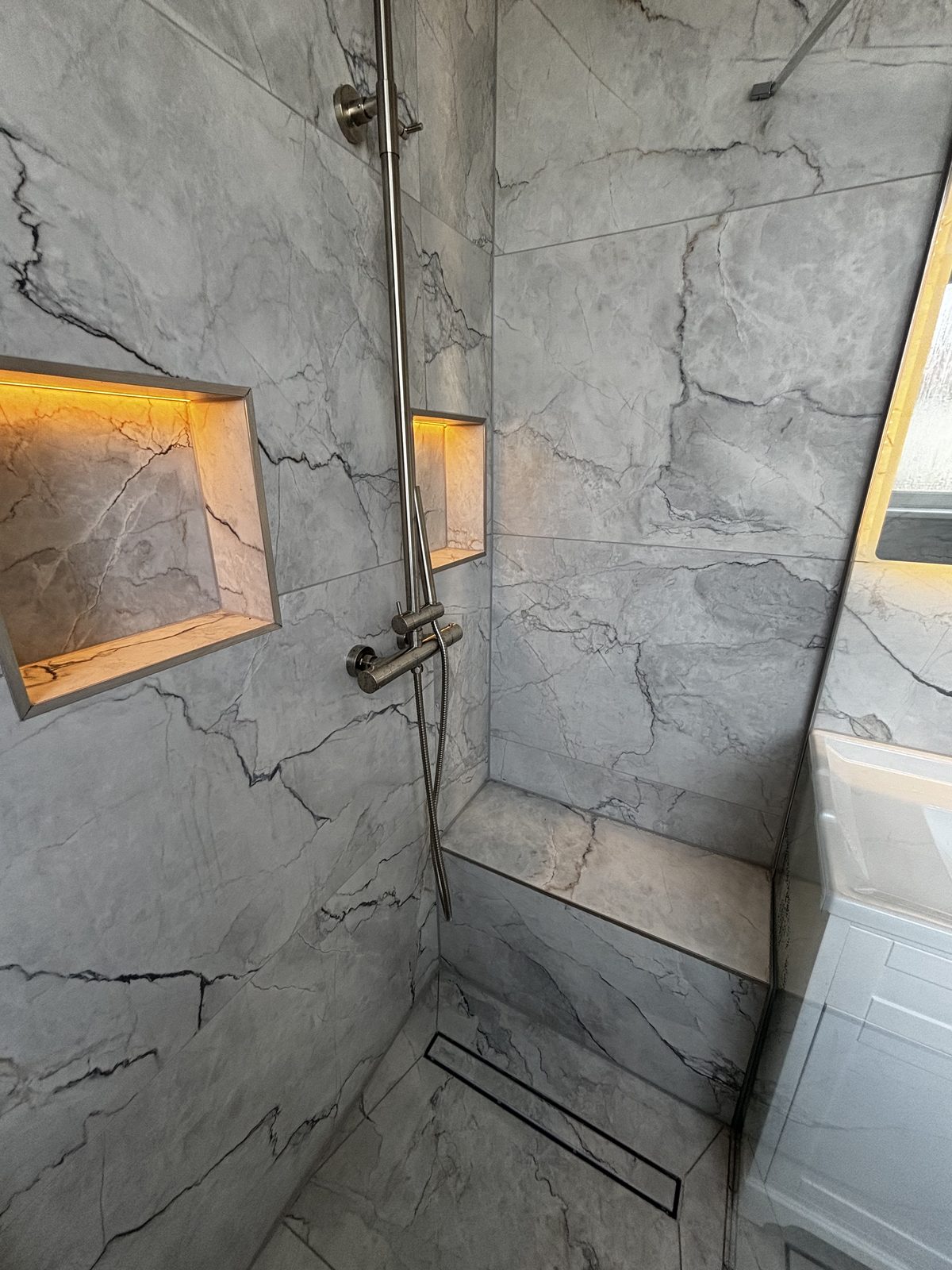 Marble-effect wet room with LED-lit niches and tiled bench seat